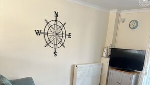 Een woonkamer met een bank, een houten salontafel, een aan de muur bevestigde televisie en een kompasdecoratie.