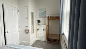 Een slaapkamer met een bed, een dressoir, een kledingkast, een hanglamp en een raam met gordijnen.