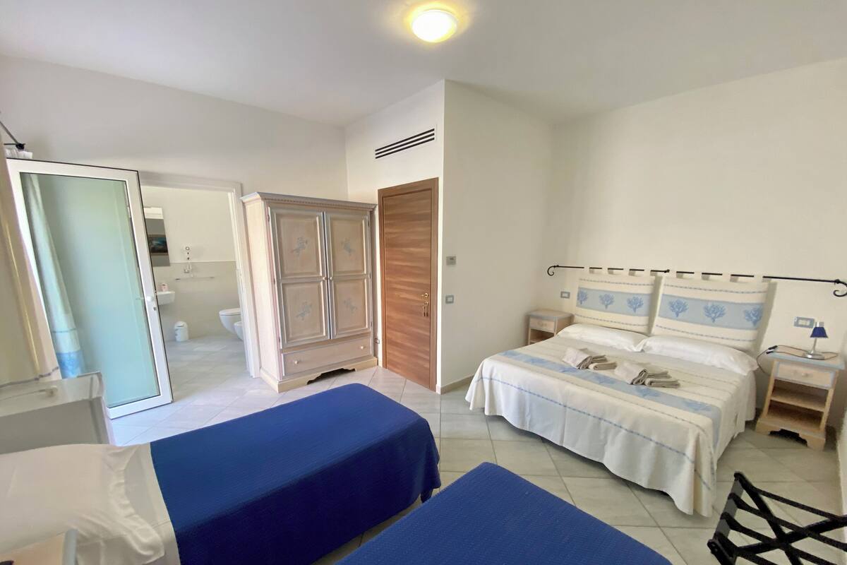 A bedroom with a bed, two bedside tables, a wardrobe, and a bathroom visible through an open door.