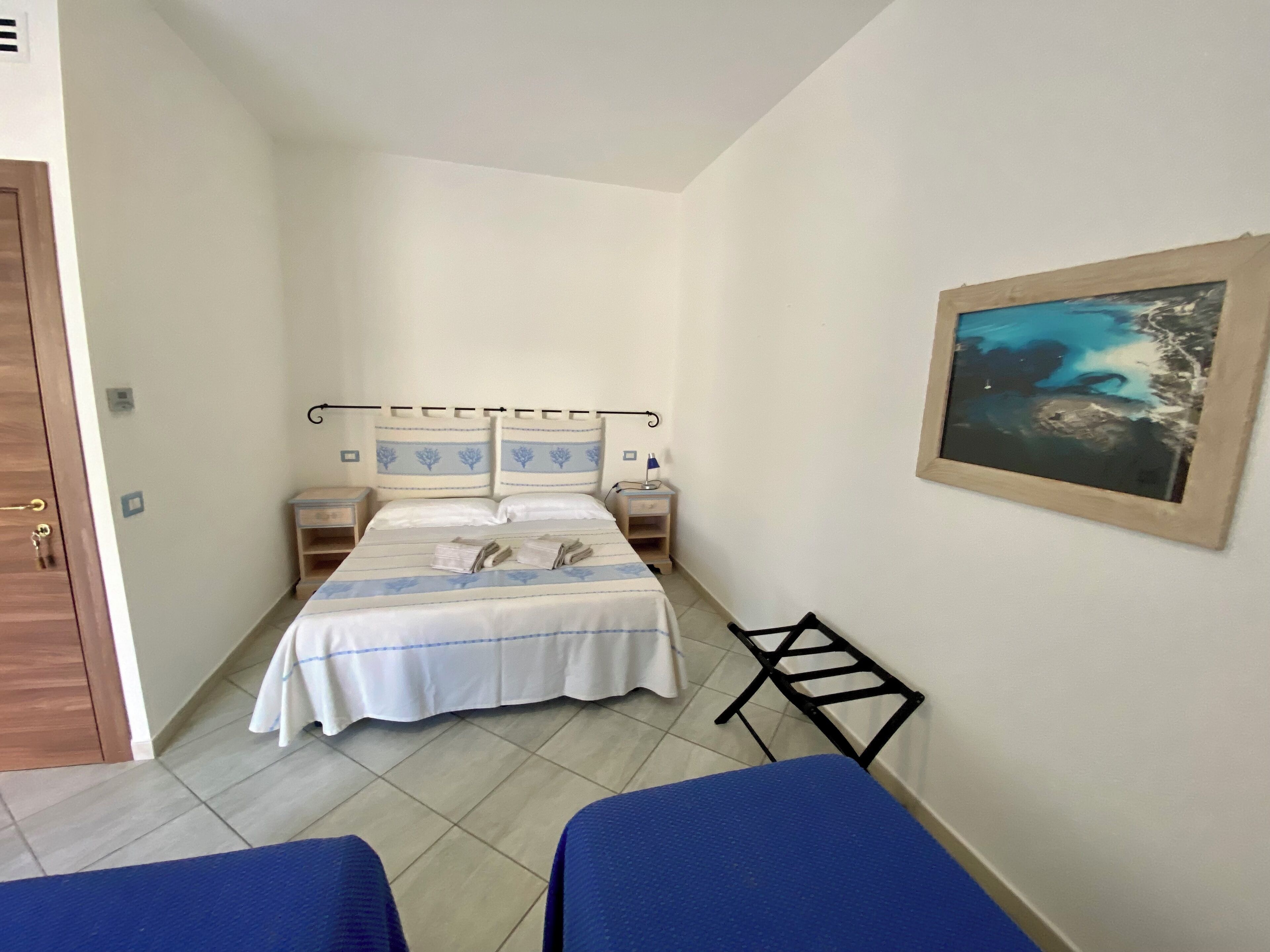 Ein kleines, schmales Hotelzimmer mit einem Bett, zwei Nachttischen, einem Schreibtisch und einem Bild an der Wand.