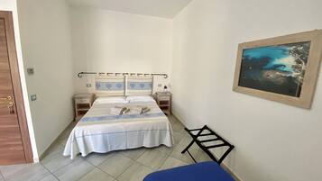 Ein kleines, schmales Hotelzimmer mit einem Bett, zwei Nachttischen, einem Schreibtisch und einem Bild an der Wand.