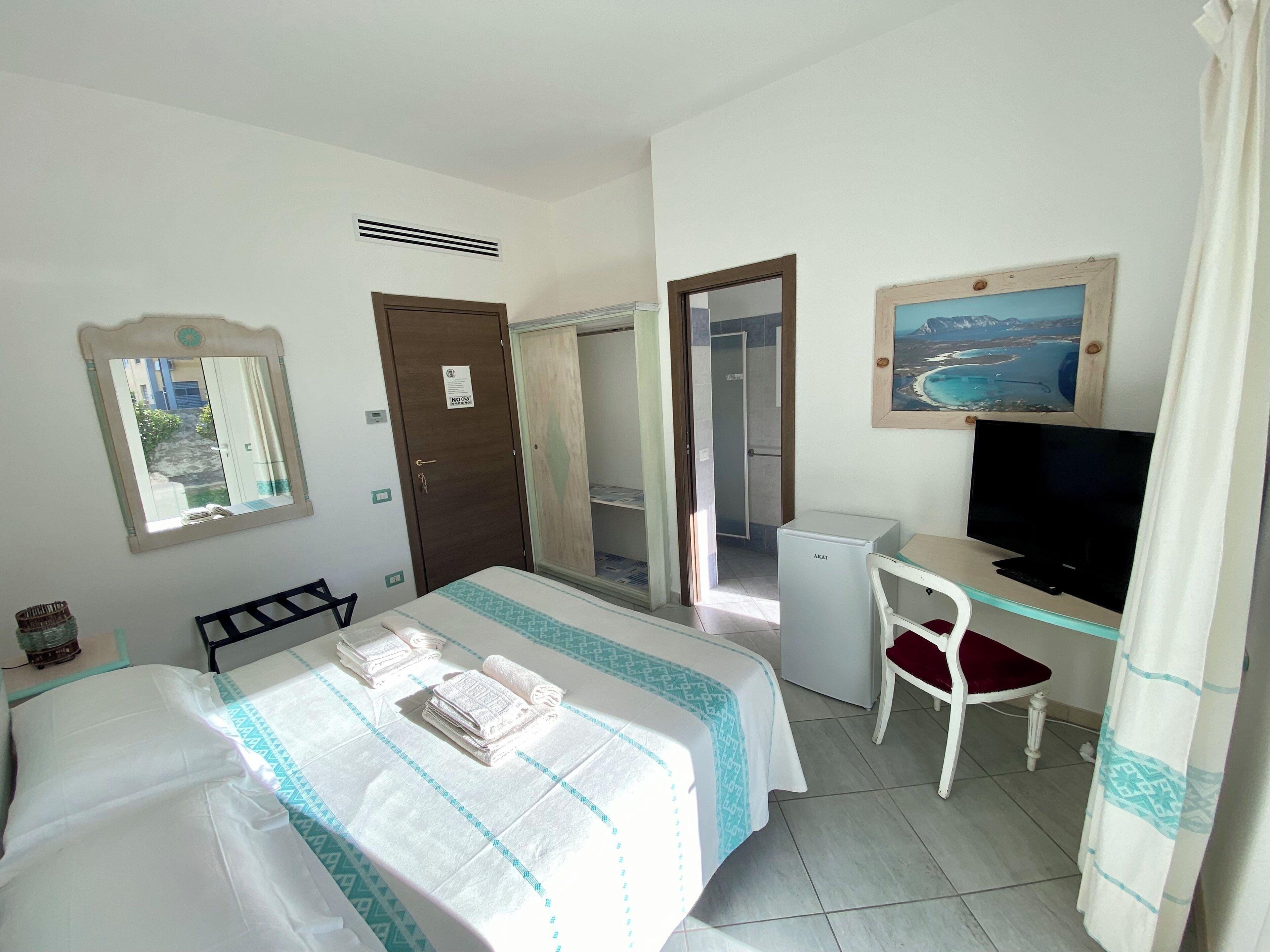 A hotel room with a bed, a desk with a chair, a television, and a painting on the wall.