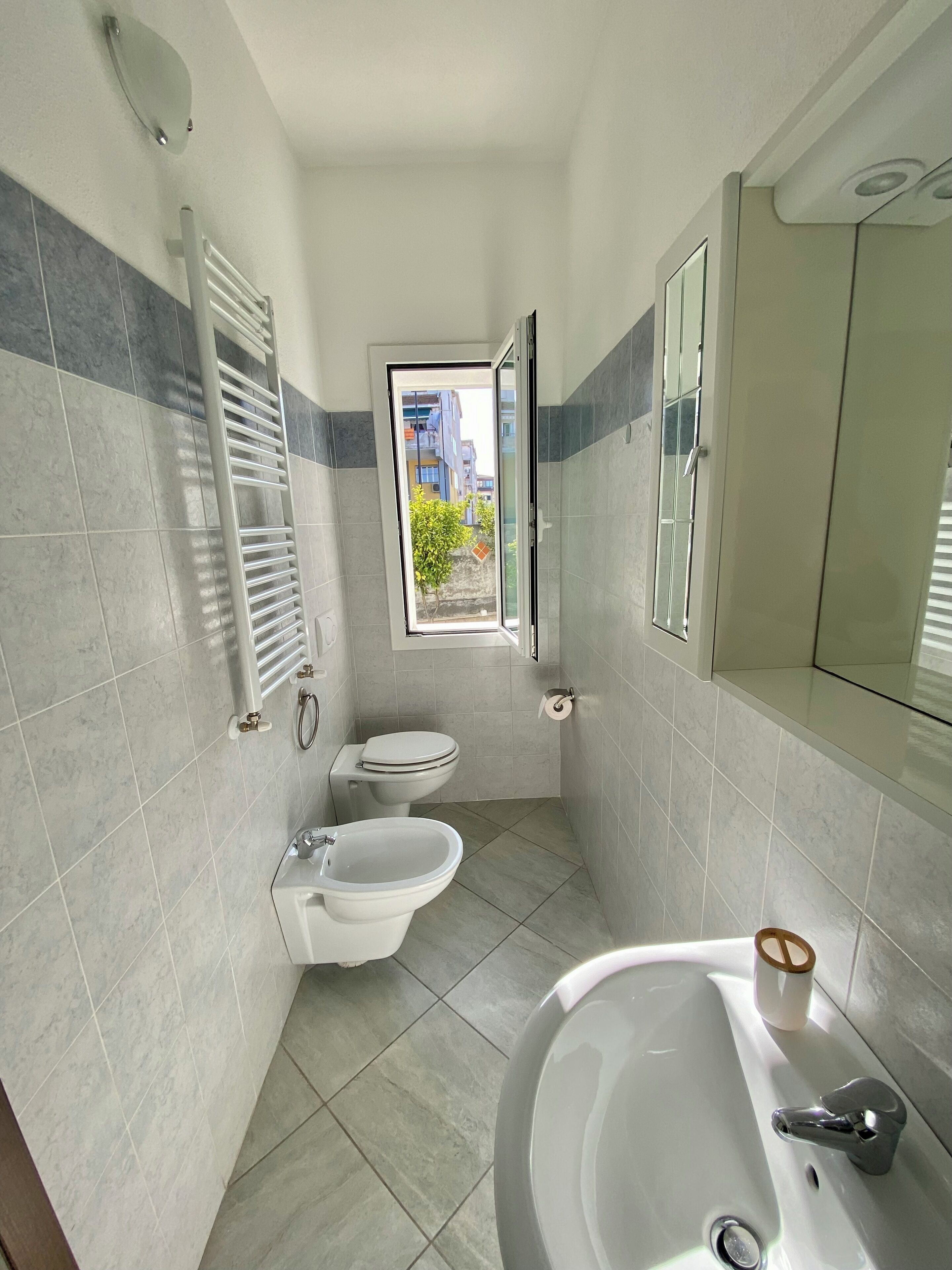 A compact bathroom with a toilet, bidet, and sink. A window provides a view of the outside.