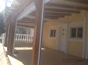 Relax under the shade of a covered outdoor area with a pergola, adjacent to a charming building with a white door and windows.