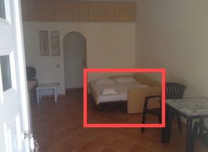 Cozy retreat with a comfortable bed, bedside table, and chair, set against a plain backdrop.