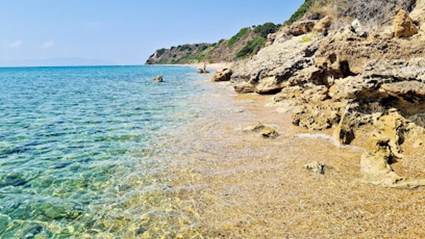 Uma praia com águas calmas e cristalinas, falésias rochosas e uma vista distante do mar.