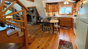 A cozy kitchen with wooden cabinets, a dining table with chairs, and a fireplace. - Granny Squirrel Getaway (Andrews)