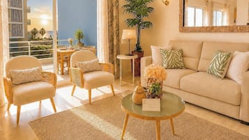 A spacious living room with a sofa, two armchairs, a coffee table, and a large window offering a view of palm trees and a building.