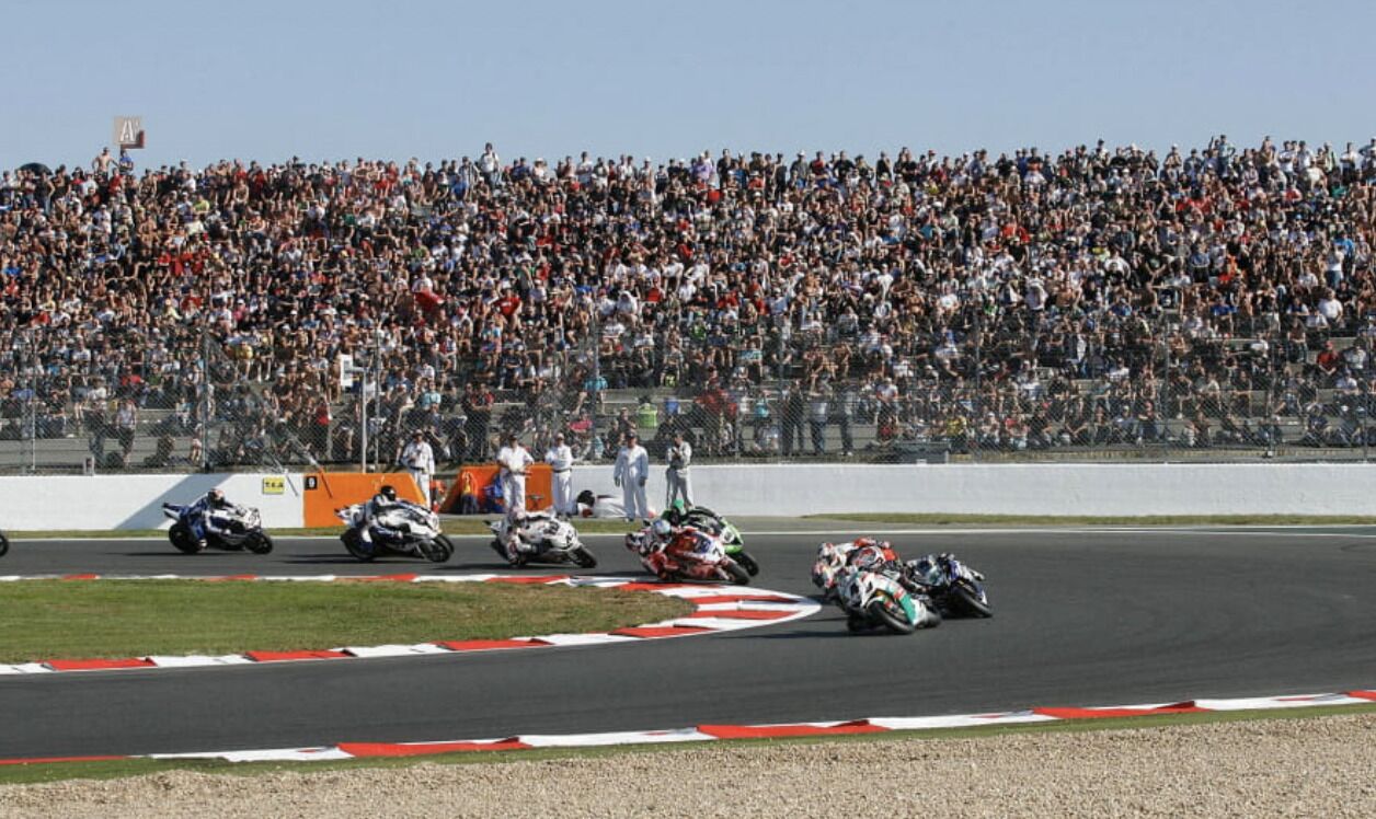 Una carrera de motocicletas en una pista, con una multitud grande al fondo.