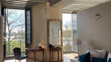 Een slaapkamer met een groot bed, een bureau, een stoel, een spiegel en een balkon met uitzicht op bomen.