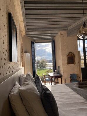 A bedroom with a large bed, a view of the outdoors, a dining table, and a chair. - Château de Meauce (Saincaize-Meauce)