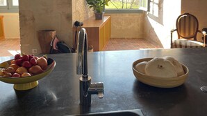 A kitchen with a sink, a bowl of fruit, and a window with a view of trees. - Château de Meauce (Saincaize-Meauce)