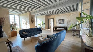 A spacious living room with exposed wooden beams, a large sofa, a coffee table, and potted plants. - Château de Meauce (Saincaize-Meauce)