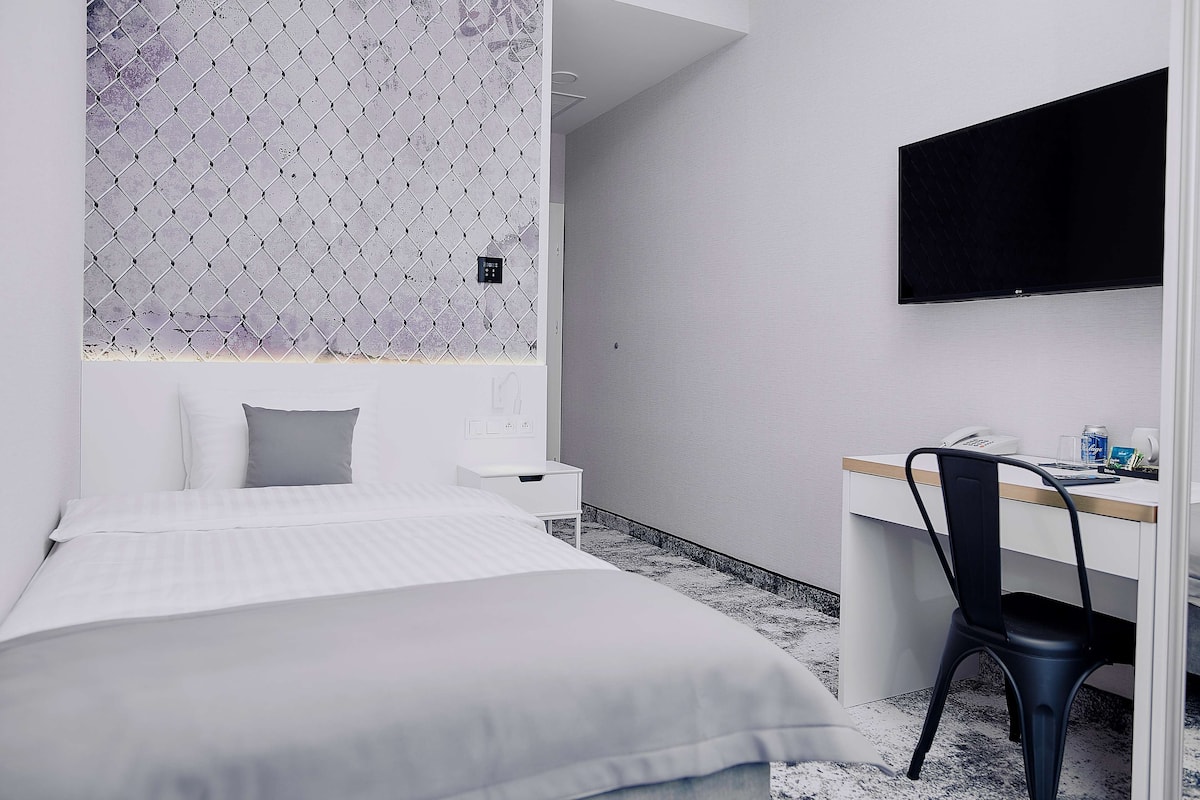 A hotel room with a bed, a desk, a chair, a TV, and a small table.
