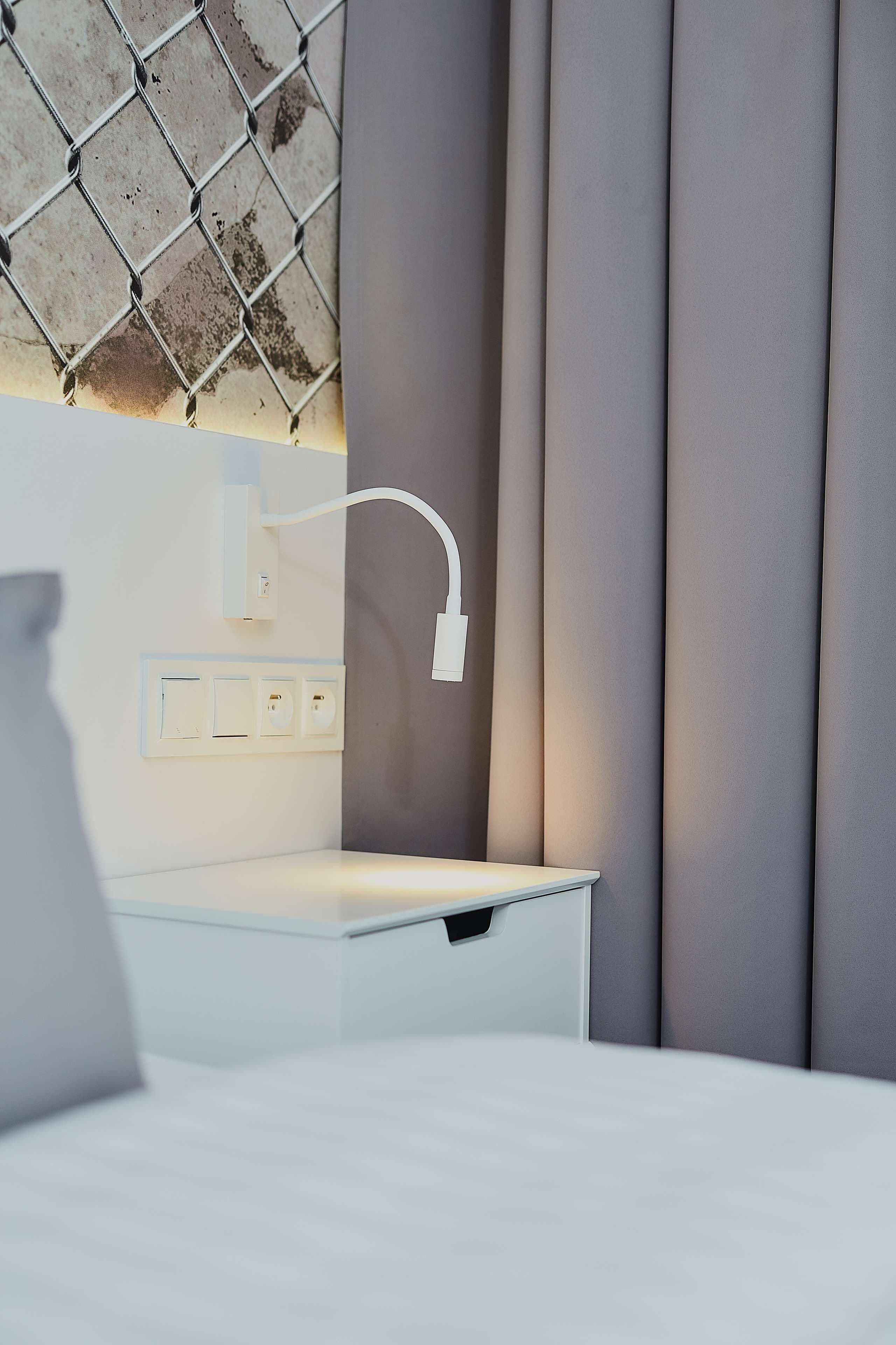 Una habitación de hotel moderna con una mesita de noche blanca, un enchufe en la pared y un sistema de gestión de cables.