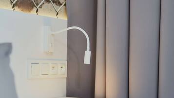 Una habitación de hotel moderna con una mesita de noche blanca, un enchufe en la pared y un sistema de gestión de cables.