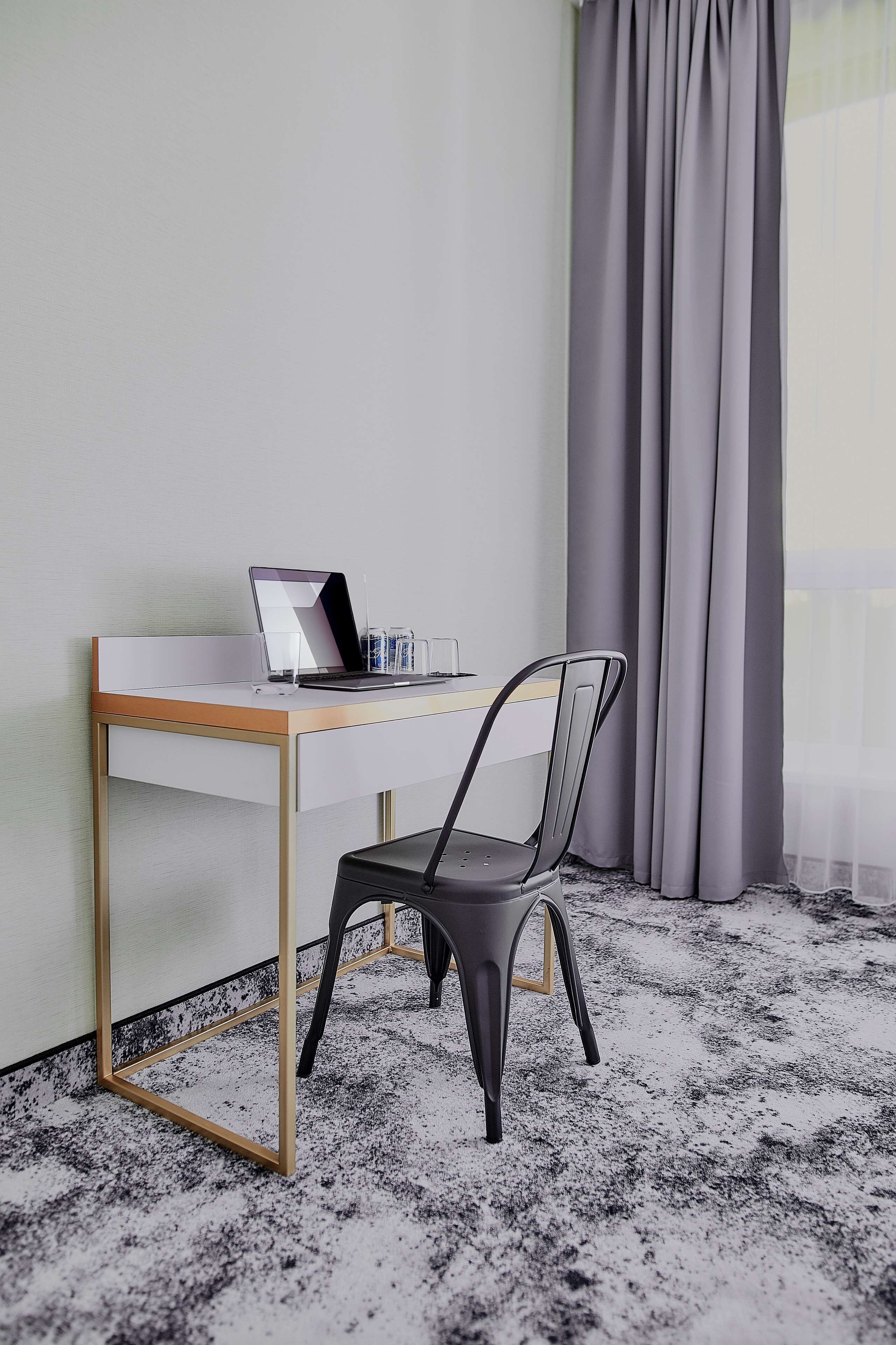 Una habitación moderna con un escritorio blanco, una laptop, una silla y una ventana con cortinas.
