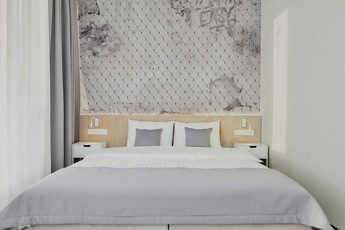A neatly made bed with a white comforter and pillows, a headboard with a patterned design, and bedside tables with lamps.