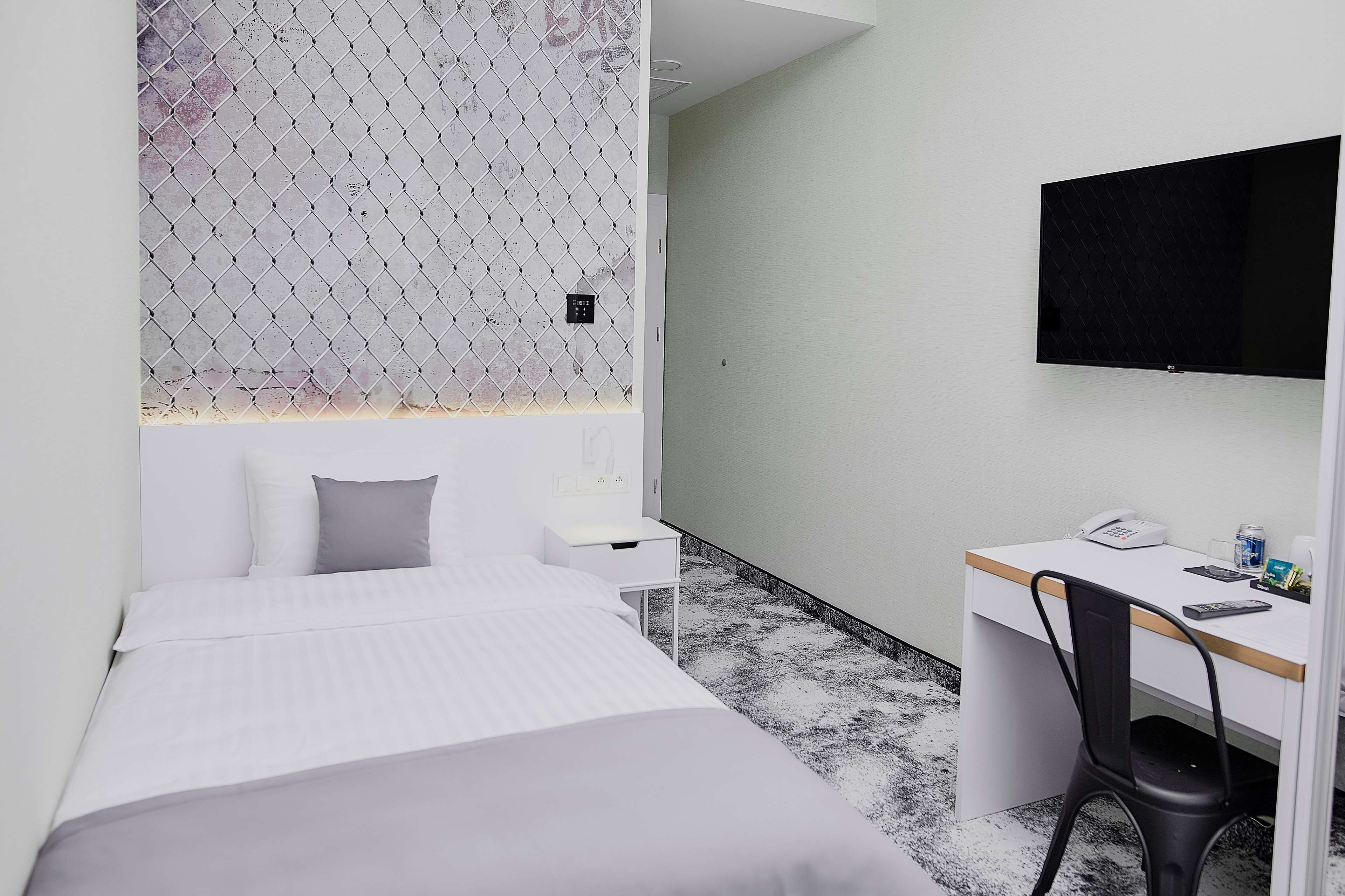 A hotel room with a bed, a desk, a chair, a TV, and a small table.