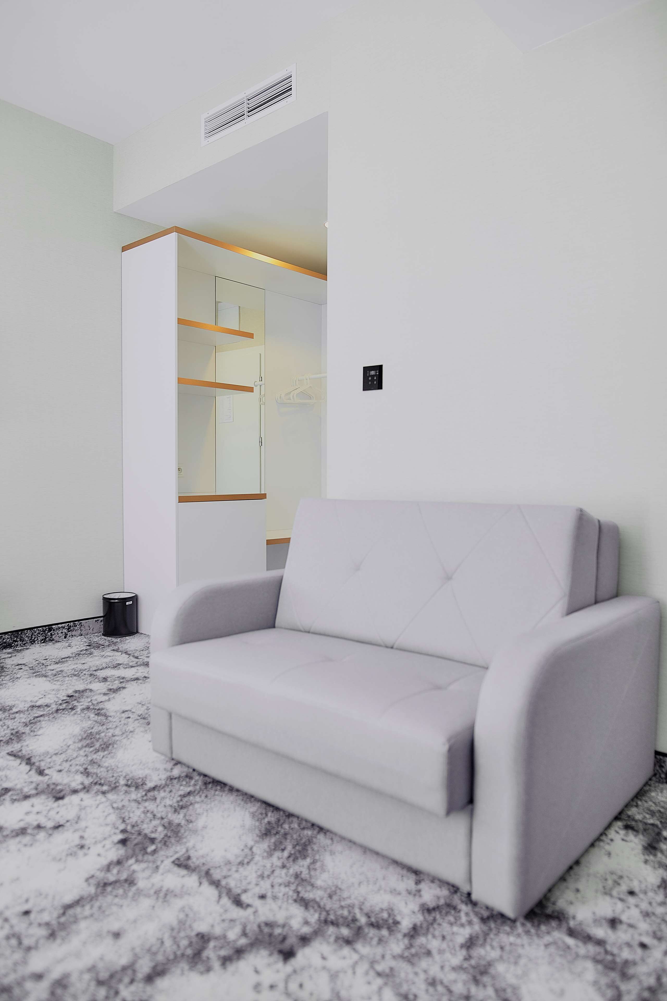 A modern room with a grey sofa, a built-in wardrobe, and a marble-patterned floor.
