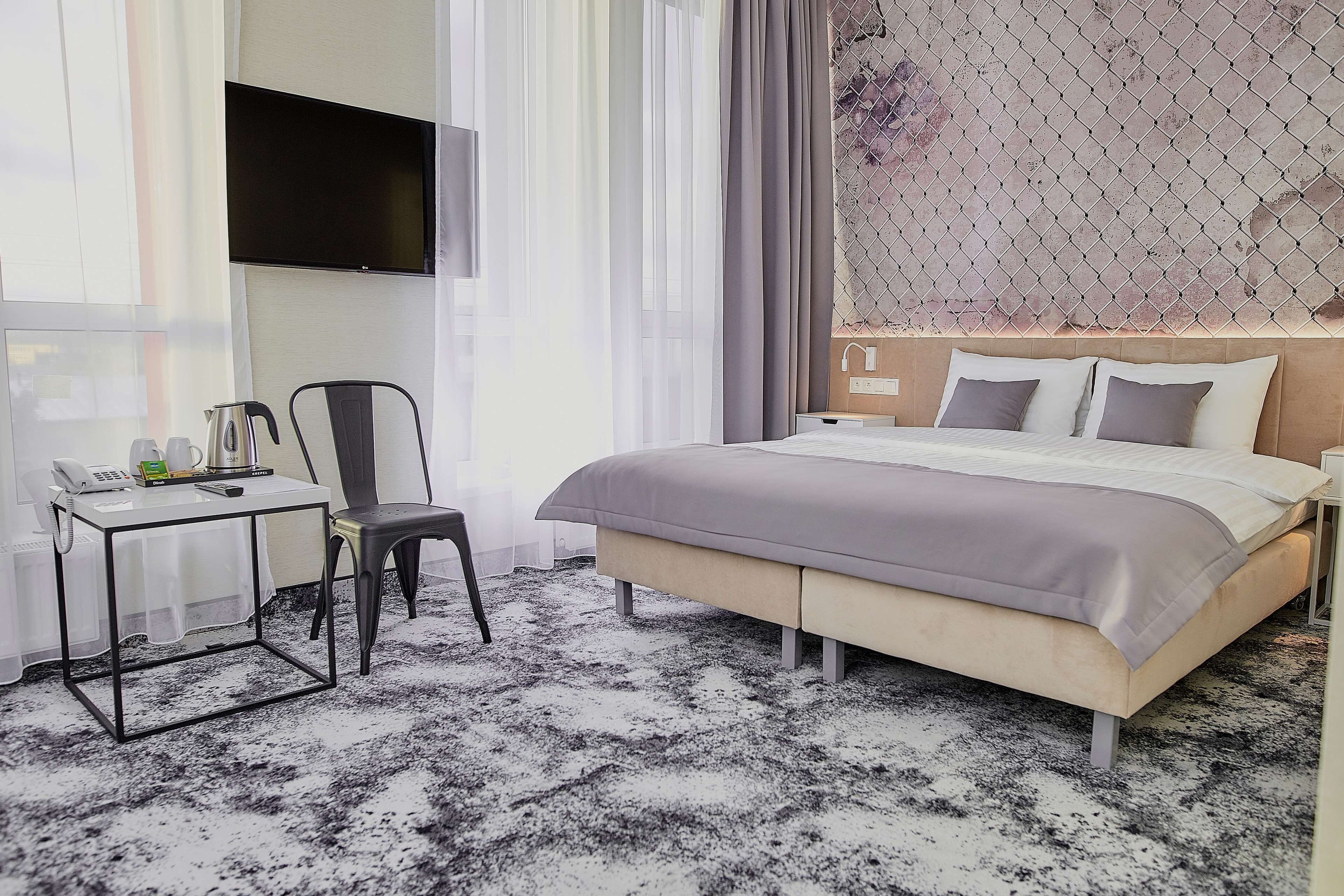 A modern hotel room with a large bed, a desk with a telephone, and a TV mounted on the wall.