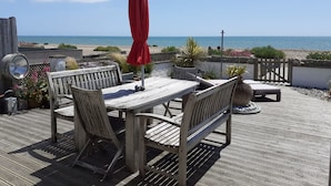 Une terrasse en bois avec une table et des chaises, un parasol rouge et une vue sur la mer.