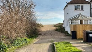 Une allée de gravier mène à une maison blanche, entourée d’une clôture en bois et dotée d’un garage.