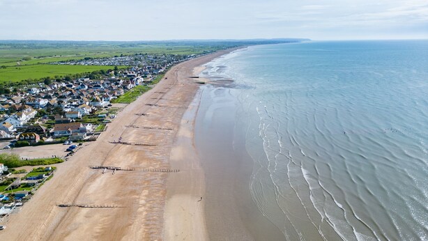 Une vue aérienne d’une ville côtière avec une longue plage de sable, des maisons le long de la côte et une vue dégagée sur l’océan.