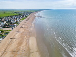 Vista aérea de un pueblo costero con una playa arenosa extensa, casas a lo largo de la orilla y una vista despejada del océano.