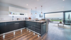 A modern kitchen with a large island, dark cabinetry, and pendant lighting. - Beach View Breeze (Pevensey)