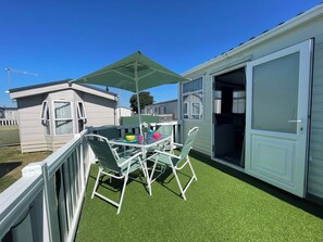 Ein überdachter Patio-Bereich mit Tisch und Stühlen, ein kleiner Tisch mit bunten Schalen und eine Glastür, die in einen Innenraum führt.