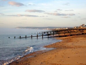 Ein Strand mit einem hölzernen Steg, der sich ins Wasser erstreckt, einem sandigen Ufer und Gebäuden im Hintergrund.