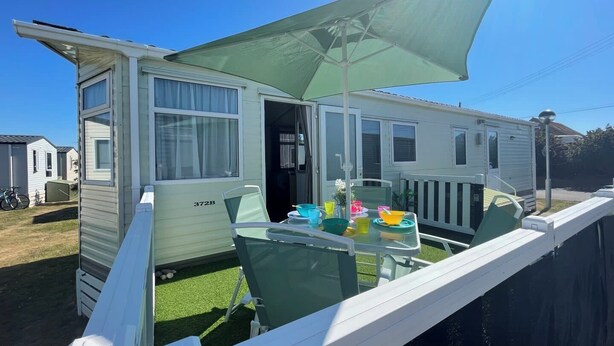 A mobile home with a patio area featuring a table and chairs, a green umbrella, and a small garden. - 27 Tower View Pevensey Bay Holiday Park Beach (Pevensey)