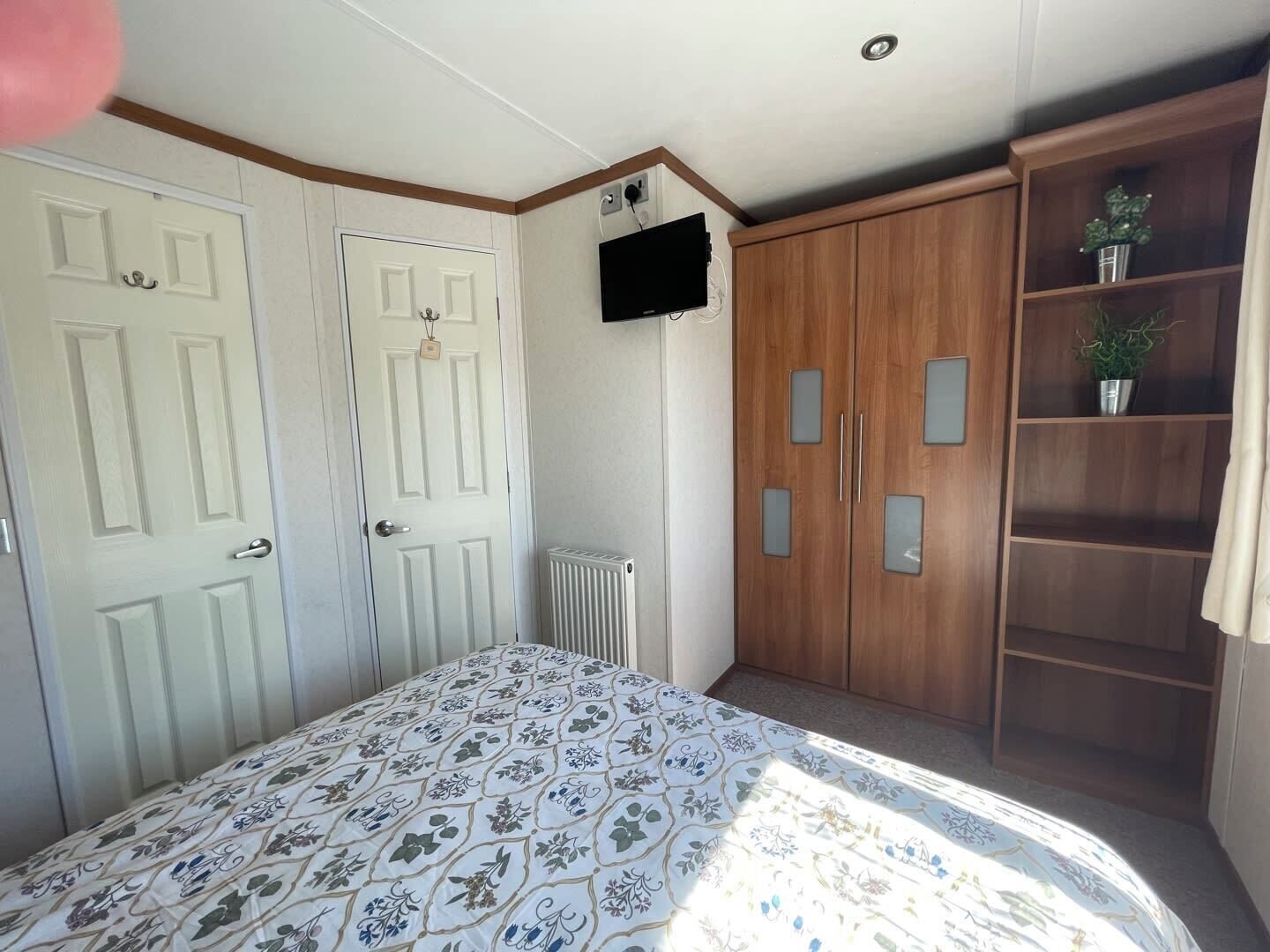 A bedroom with a bed, two white doors, a wooden wardrobe, and a radiator.