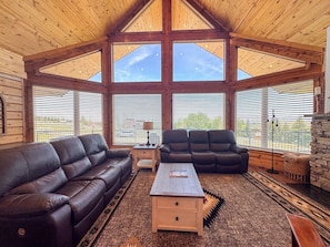 A spacious living room with a high ceiling, large windows, a fireplace, and leather sofas. - Nature Calls- New home, hot tub & Ideal Beach Pass (Garden City)