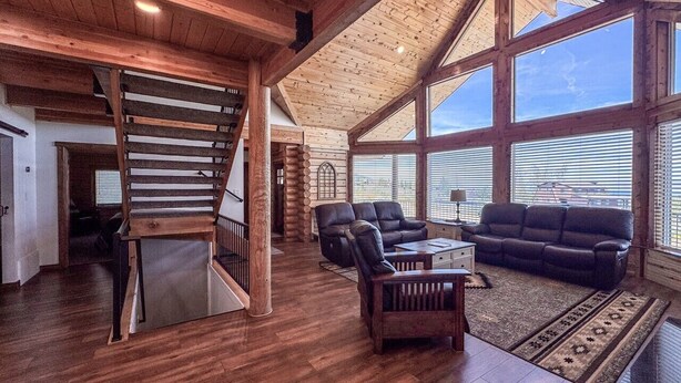 A spacious living area with a wooden staircase, leather sofas, and large windows. - Nature Calls- Log home, hot tub & Ideal Beach Pass (Garden City)