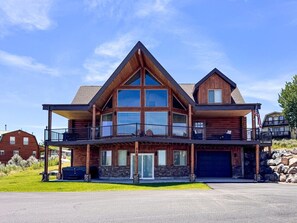 Une grande cabane en rondins à deux étages, dotée d’un balcon, d’un garage et de fondations en pierre.