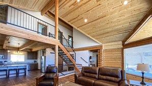 A spacious living area with a wooden ceiling, a staircase, a kitchen, and a seating area with leather sofas. - Nature Calls- Log home, hot tub & Ideal Beach Pass (Garden City)