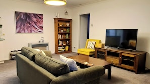 Ein Wohnzimmer mit einer Couch, einem Couchtisch, einem Bücherregal, einem Fernseher und einer Lampe.