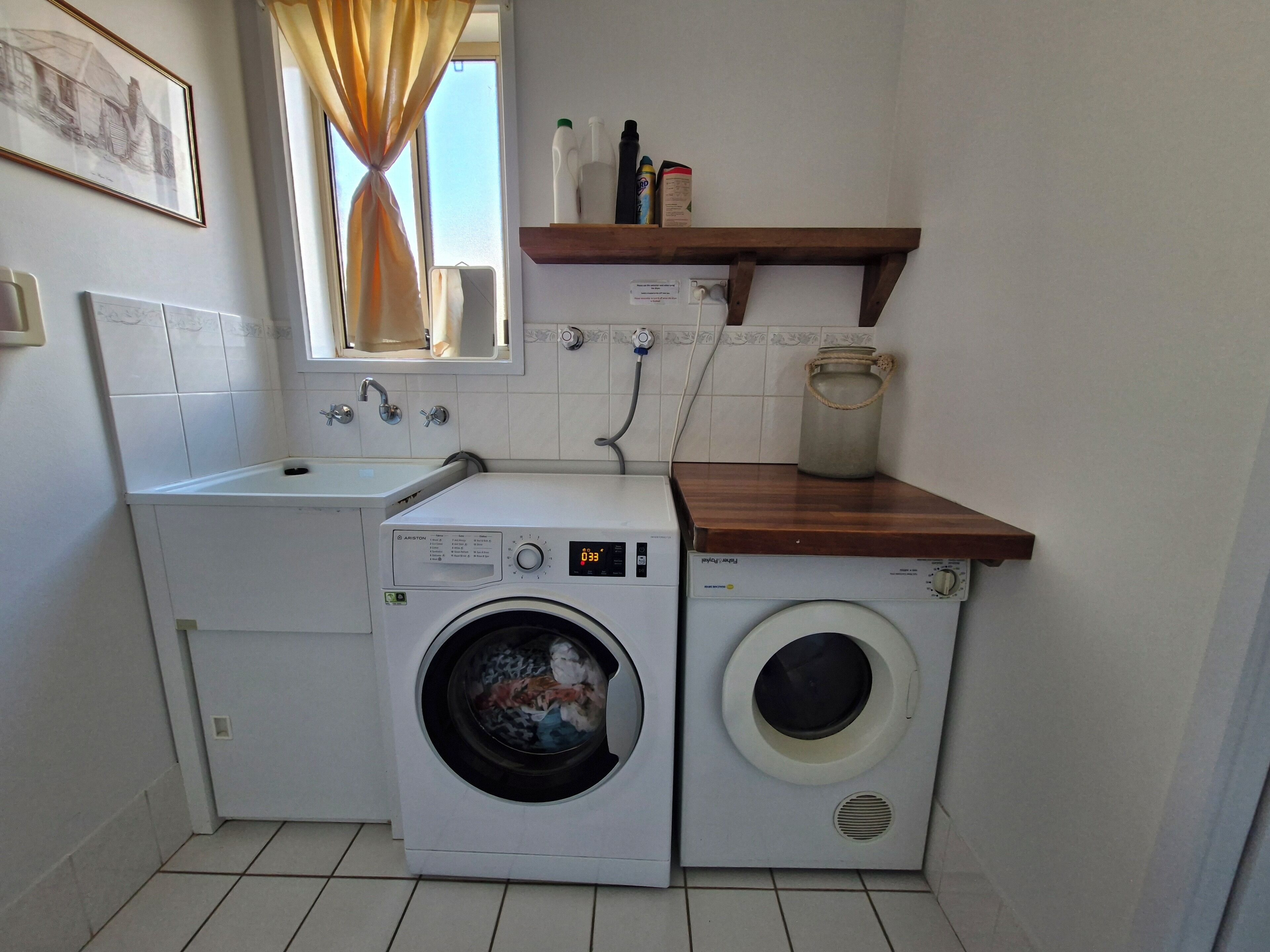 Pequeña lavandería con lavadora y secadora, un lavamanos y un estante con productos de limpieza.