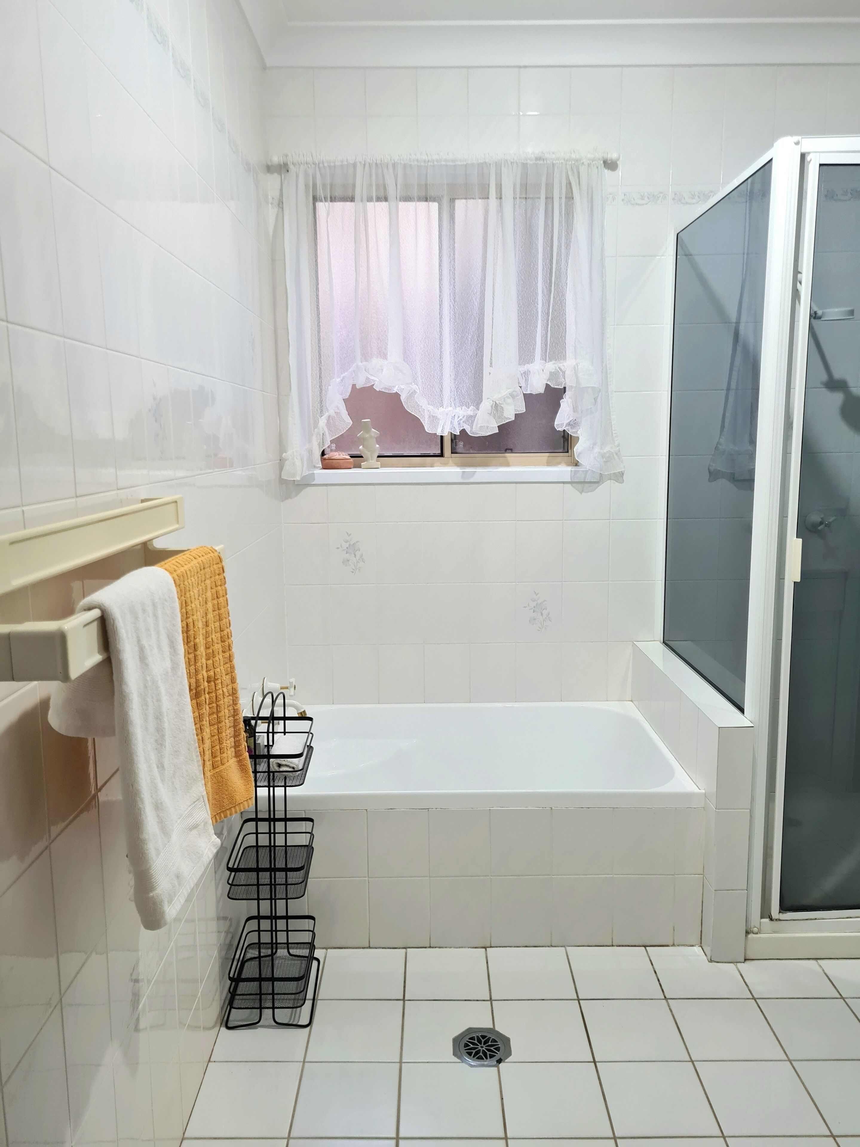 Une salle de bain avec une baignoire, une fenêtre avec un rideau léger, un porte-serviettes avec des serviettes et un espace douche.