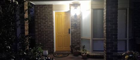 A brick house with a wooden front door, a small porch, and potted plants.