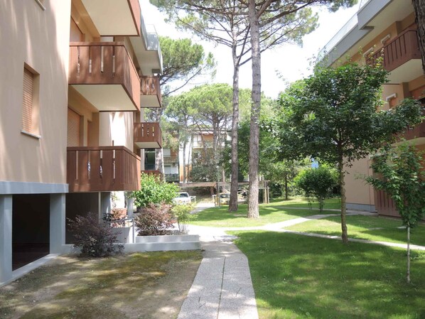 A courtyard with a pathway, trees, and a building with balconies.