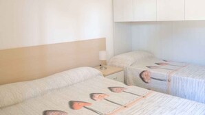 Una habitación de hotel con dos camas, una mesita de noche con lámpara y un armario.