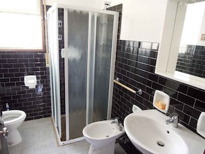 A bathroom with a glass shower enclosure, a toilet, and a sink with a mirror above.