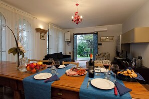 Un coin repas avec une table en bois dressée pour le repas, un lustre et une vue sur le jardin.