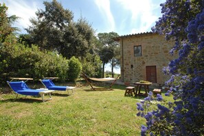 Un bâtiment en pierre avec un hamac et des chaises longues bleues, le tout situé dans un espace verdoyant.
