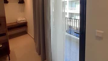 A hotel room with a balcony, a bed with a headboard, a bench, and a coat rack.
