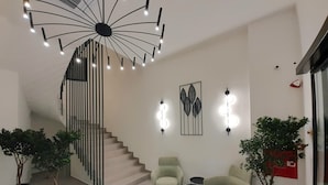 Un interior moderno con una escalera de caracol, una zona de estar con dos sillones y una pequeña mesa, y apliques decorativos en la pared.