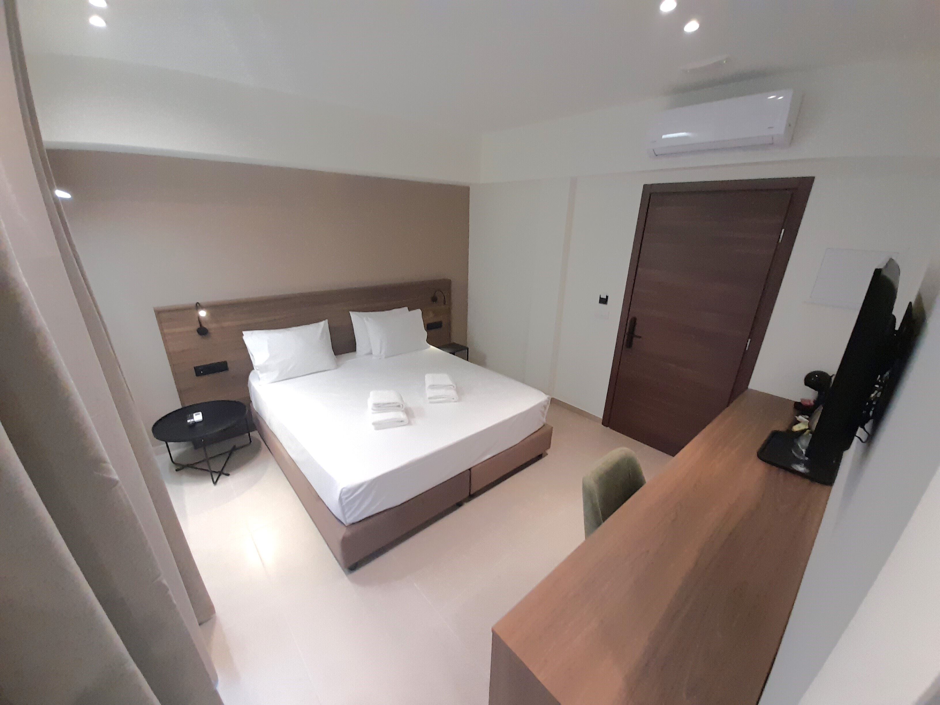 Una camera d'albergo con un letto, comodino, scrivania, sedia e una porta.